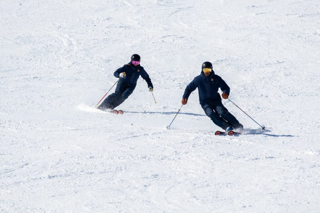 Two Far East Snowsports instructors carving side by side during training